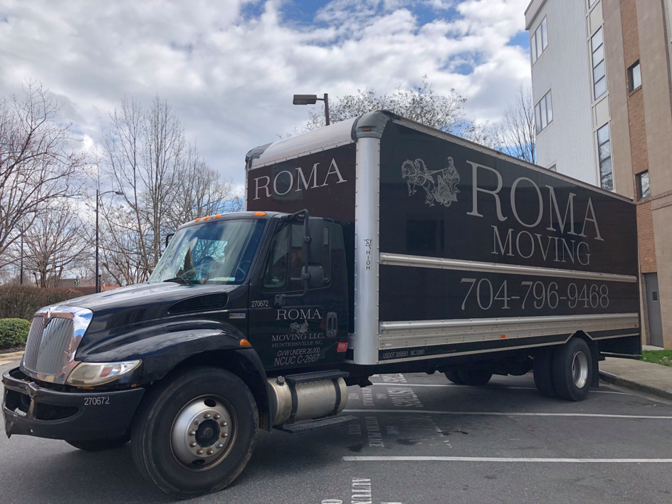 A Roma Moving truck parked in a commercial parking lot under a cloudy sky in Charlotte, NC.