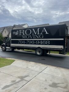 A Roma Moving truck parked on a residential street under a cloudy sky in Charlotte, NC.