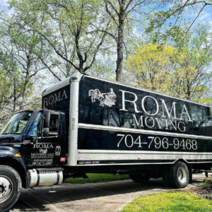 A black Roma Moving truck with the company logo and phone number parked under trees in Charlotte, NC.