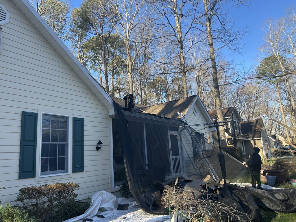 Workers performing a roof replacement project with protective tarps on the ground by PJ Fitzpatrick LLC in New Castle, DE, often for water damage.