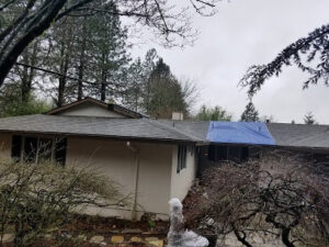 A house with a blue tarp on the roof, indicating storm or water damage repair by PacWest Restoration in Tigard, OR