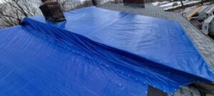 A blue tarp covering a damaged roof to prevent further water intrusion, installed by Clean Care of New England in Cranston, RI
