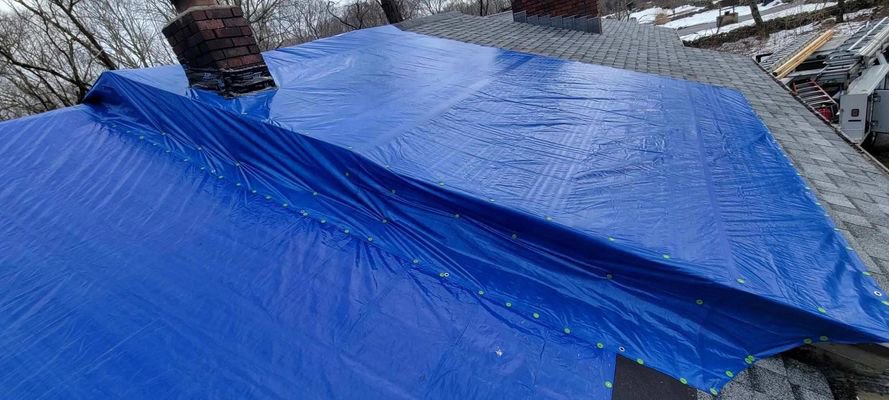 A blue tarp covering a damaged roof to prevent further water intrusion, installed by Clean Care of New England in Cranston, RI