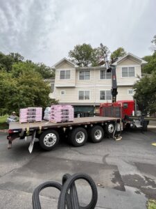 A truck delivering roofing materials to a house with light-colored siding, indicating exterior work by Archcraft Exteriors in South Saint Paul, MN.