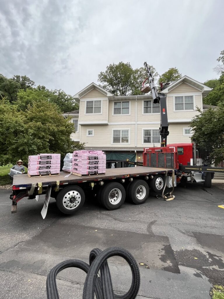 A truck delivering roofing materials to a house with light-colored siding, indicating exterior work by Archcraft Exteriors in South Saint Paul, MN.