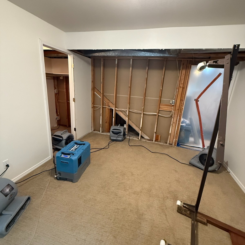 A room with exposed wall studs and drying equipment after water damage restoration by Peak Performance Restoration in Meridian, ID.
