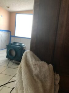 A room with an air mover and blue tape on the walls, indicating water damage restoration work by Southcoast Cleaning Solutions & Restoration in Fall River, MA.
