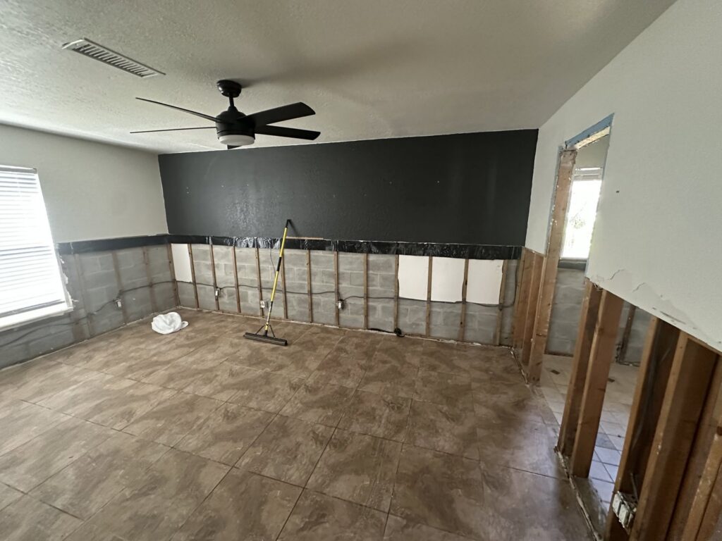 A room with lower drywall removed, exposing studs and concrete blocks with plastic sheeting for water damage remediation by Catalyst Restoration in Hagerstown, MD.