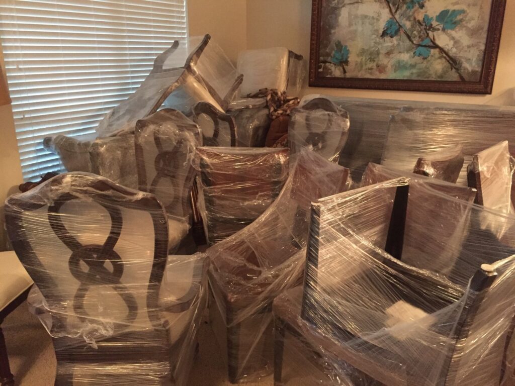A room filled with various pieces of furniture, professionally wrapped in plastic and ready for moving by Kingdom Men Movers in Houston, TX.
