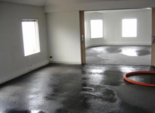 A room with a dark, wet floor and an orange hose, showing water damage in Oakland, CA by One Call Services of Oakland.