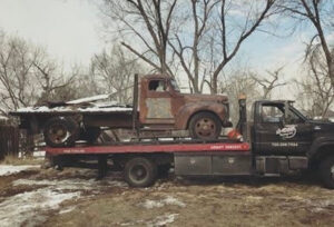 A rusty old truck being transported on a flatbed tow truck by A-ROD Towing in Denver, CO.