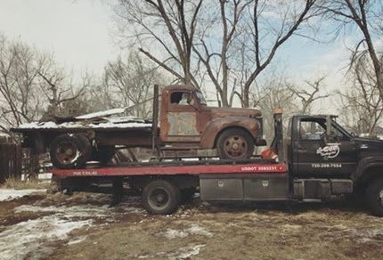 A rusty old truck being transported on a flatbed tow truck by A-ROD Towing in Denver, CO.