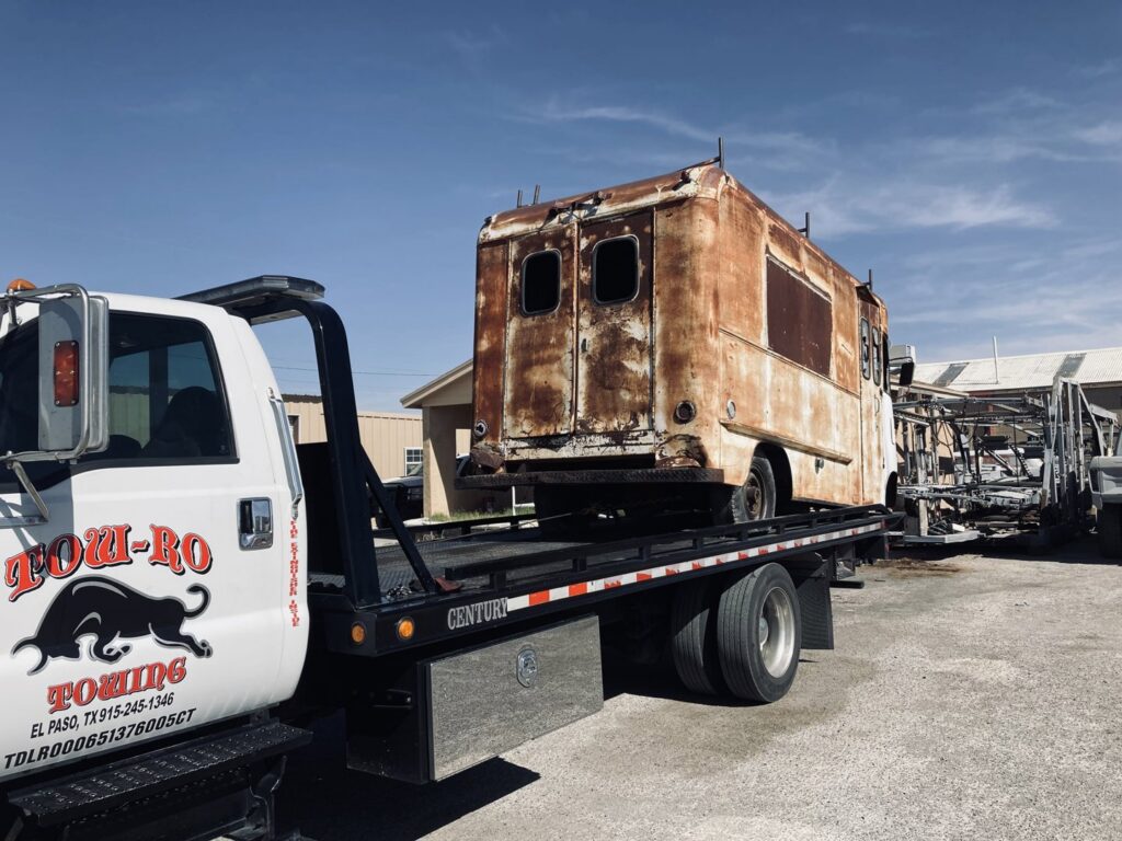A rusty utility truck being transported on a flatbed tow truck by Tow-Ro Towing in El Paso, TX.