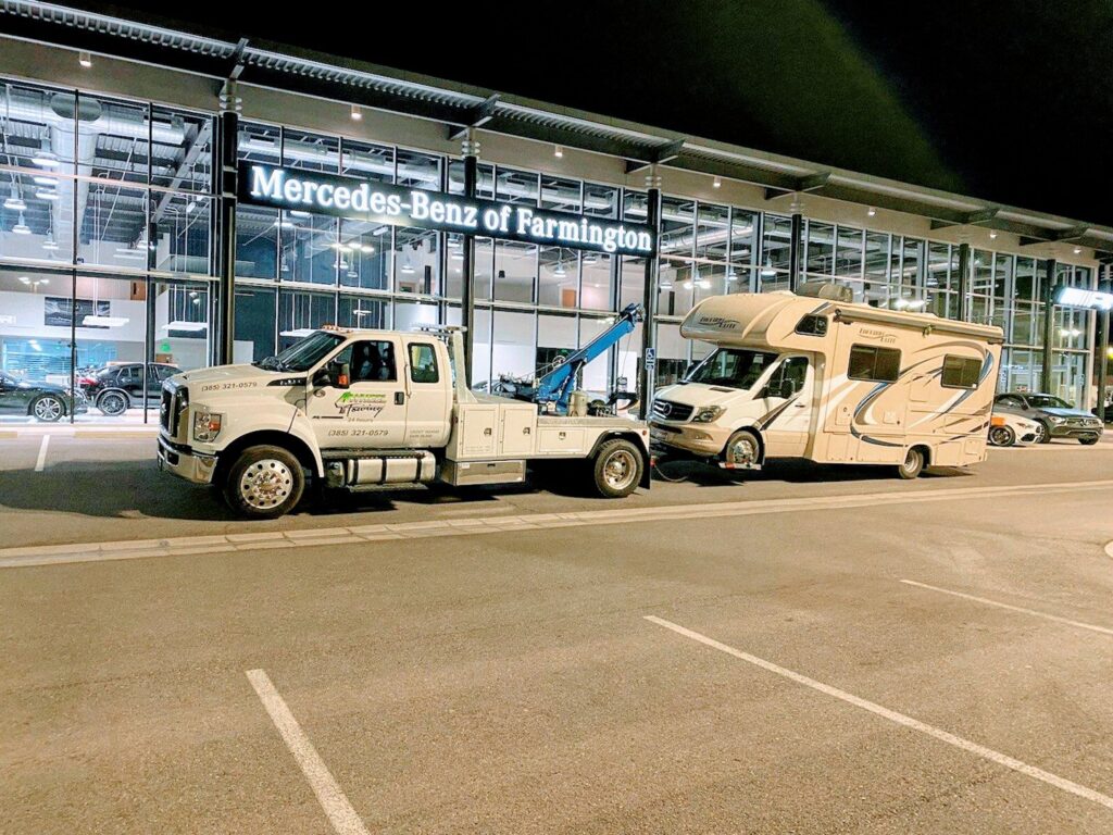 A large RV motorhome being towed by a 4 Wheel Towing truck from a Mercedes-Benz dealership in South Salt Lake, UT.