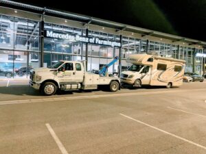 A large RV motorhome being towed by a 4 Wheel Towing truck from a Mercedes-Benz dealership in South Salt Lake, UT.