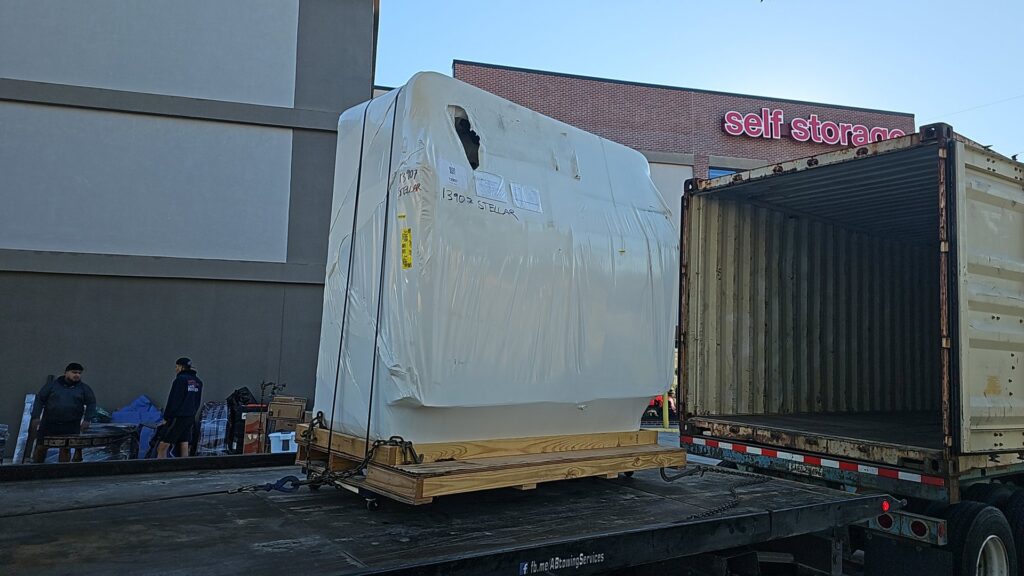 A large yellow RV or motorhome being transported on a flatbed tow truck by AB Towing & Transport in San Antonio, TX.