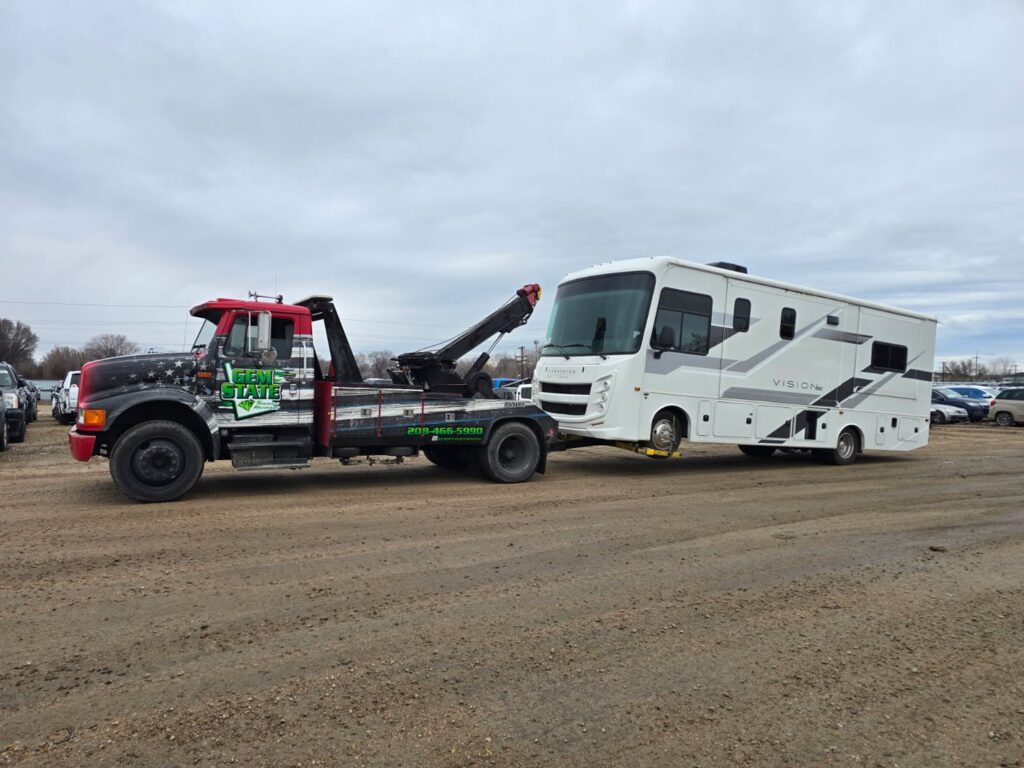 A large RV being towed by a heavy-duty wrecker from Gem State Towing and Recovery in Caldwell, ID.