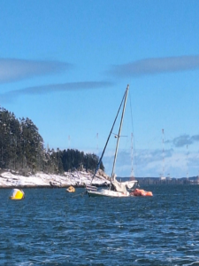 A sailboat in distress, partially submerged in open water, awaiting towing services from Downeast Marine Towing, LLC in Eastport, ME.
