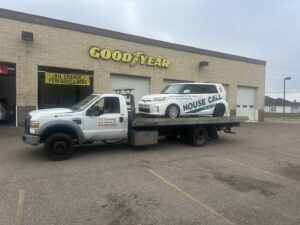 TJ Towing LLC flatbed truck towing a white Scion xB from a Goodyear service center in New Orleans, LA.