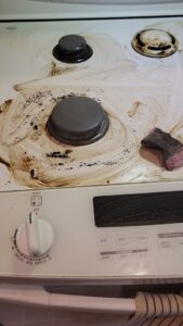 A gloved hand actively scrubbing a dirty stove top, part of a deep kitchen clean by Solange D Kleaner in New Bedford, MA.