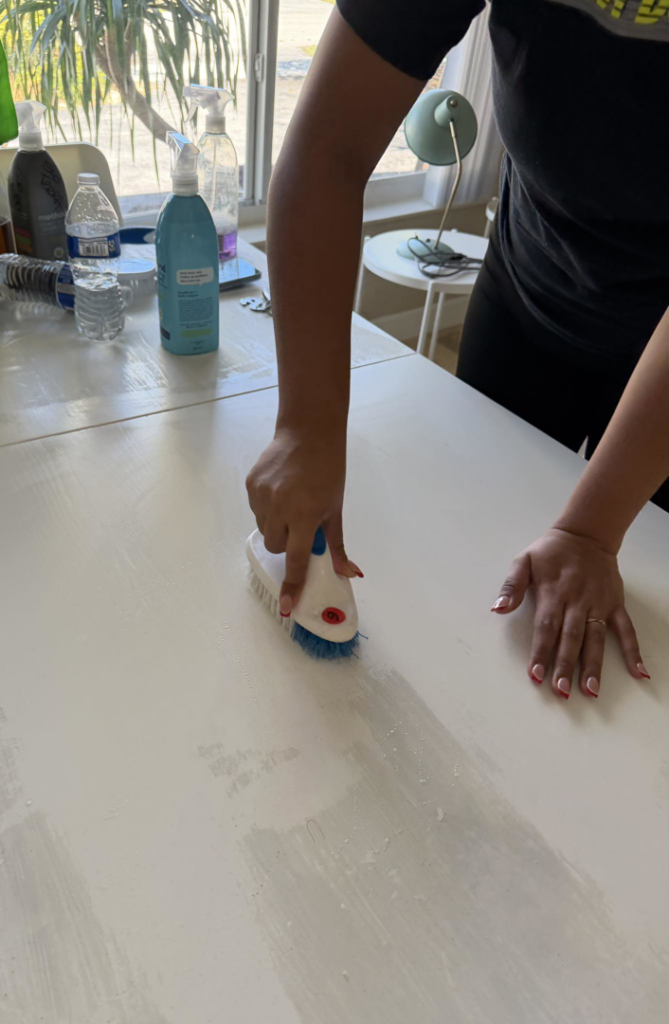 Hands scrubbing a white table with a cleaning brush, showing a detailed cleaning service by Eco-Terra Clean in Fort Lauderdale, FL.