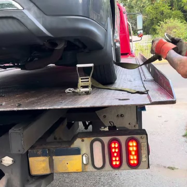 A person securing a car tire with a strap on a flatbed tow truck, performing a towing service for Fort Benning Towing in Columbus, GA