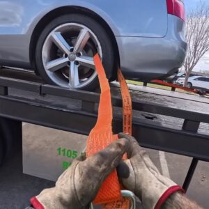 Gloved hands securing a car wheel with a strap on a flatbed tow truck by Columbus Towing in Columbus, GA.
