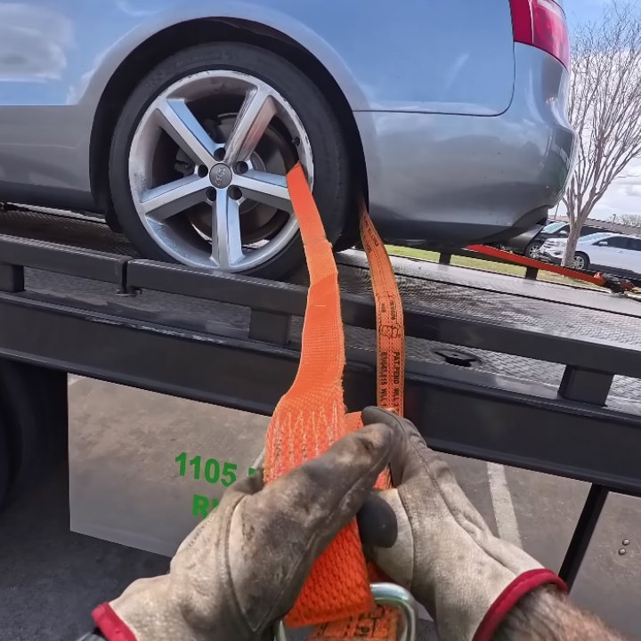 Gloved hands securing a car wheel with a strap on a flatbed tow truck by Columbus Towing in Columbus, GA.