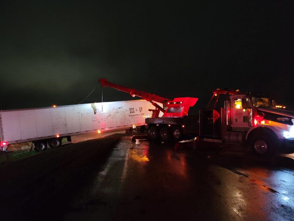 A CC Wrecker Service rotator truck performing a semi-trailer recovery on a road at night in Corpus Christi, TX.
