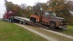 A semi-truck with a flatbed trailer from Tally's Towing and Recovery loading a rusty vintage pickup truck in Owensboro, KY.