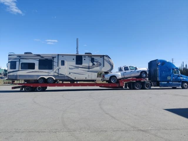 A semi-truck from Help Line Towing transporting a large RV and a pickup truck on a flatbed trailer in Wasilla, AK.