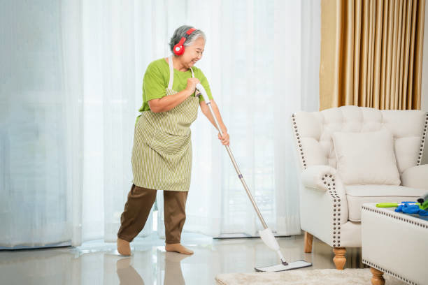 A senior woman wearing headphones and mopping a floor in a living room, depicting professional house cleaning by Cascade Fresh Cleaning Services in Grand Rapids, MI.