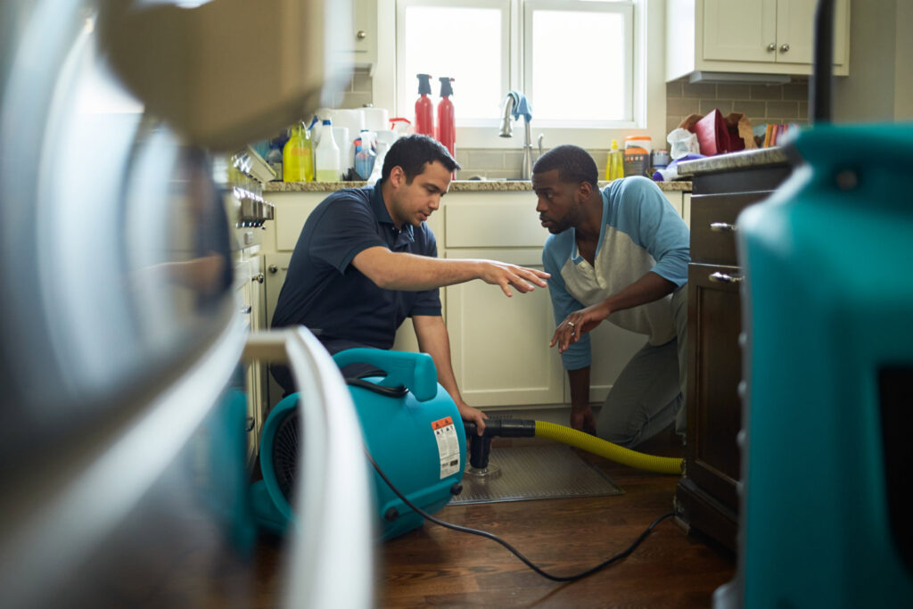 A ServiceMaster DSI employee discussing water damage restoration with a homeowner, with drying equipment visible in Maple Grove, MN.