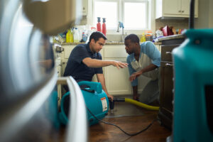 A ServiceMaster DSI employee discussing water damage restoration with a homeowner, with drying equipment visible in Maple Grove, MN.