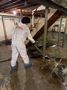A Servpro technician in a hazmat suit extracting dirty water from a flooded basement floor in New Bedford, MA