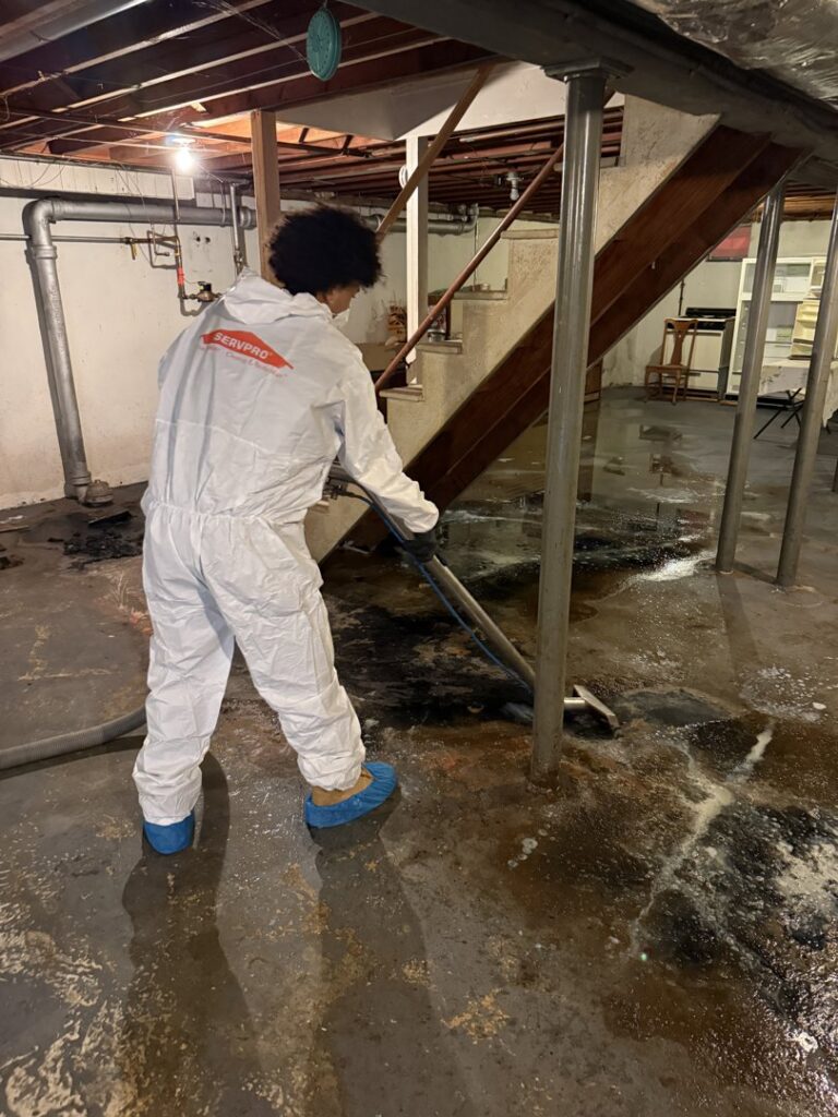 A Servpro technician in a hazmat suit extracting dirty water from a flooded basement floor in New Bedford, MA