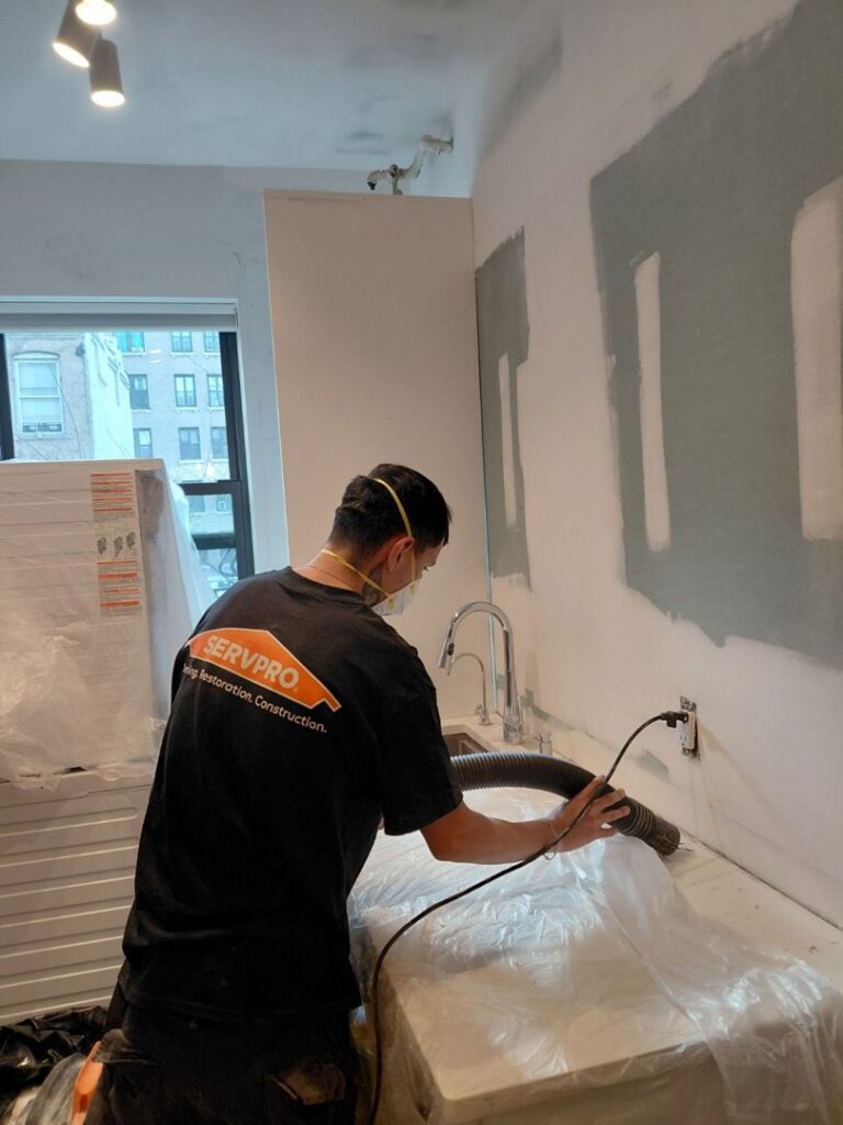 A Servpro worker vacuuming a countertop area covered in plastic for Servpro of SW Onondaga County in Syracuse, NY.