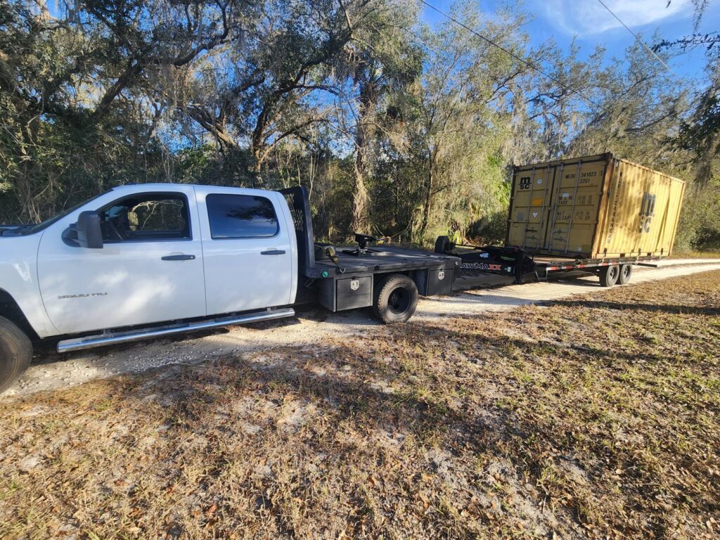 A shipping container on a trailer being towed by a pickup truck from Tiki's Towing LLC in Jacksonville, FL.