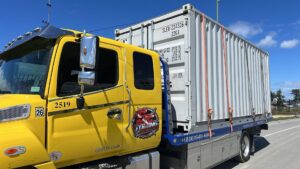 A large shipping container is being transported on a flatbed tow truck by S&F Towing in Oakland, CA.
