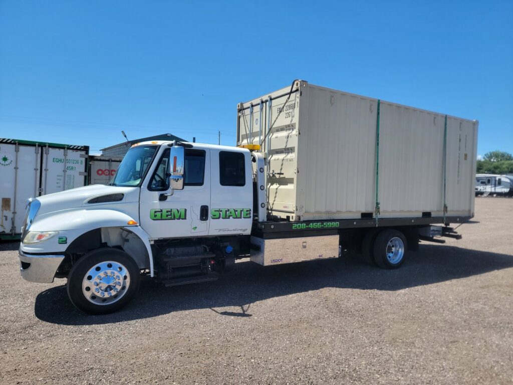 A shipping container being transported on a flatbed tow truck by Gem State Towing and Recovery in Caldwell, ID.