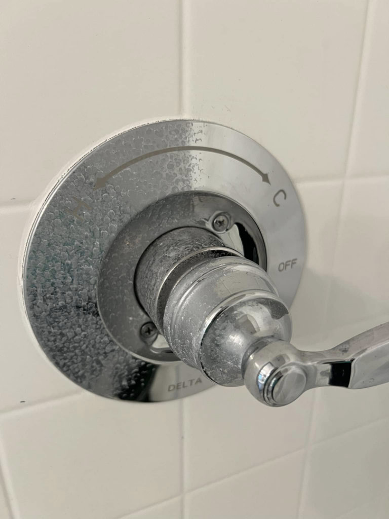 A shower faucet showing hard water stain removal in progress by Idaho Gem Cleaning in Caldwell, ID.