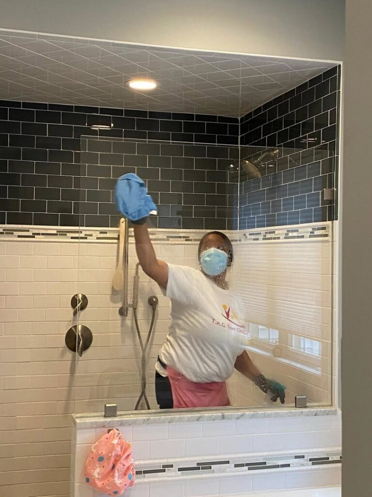 A house cleaner wiping down a shower glass door in a bathroom for TAG Team Cleaning of West Hartford, CT