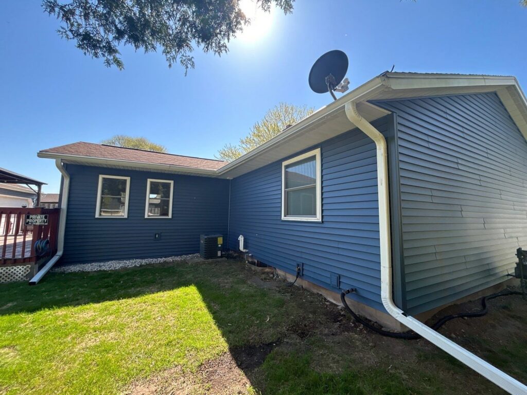 The side of a house showcasing new dark blue siding and white gutters installed by Wisconsin Exteriors in Kaukauna, WI.