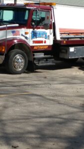 Side view of a flatbed tow truck from Bailey's Towing and Auto Body, LLC parked in Merrimack, NH.