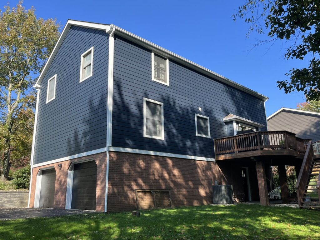 A side view of a house showcasing new dark blue siding and a brick foundation by My Guys Remodeling Experts in Bethel Park, PA.