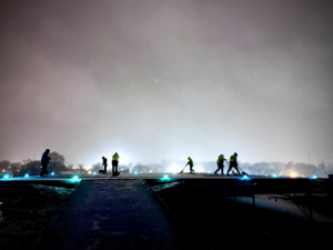 A sidewalk crew from Snow & Ice Management Company shoveling snow on a walkway at night in Pittsburgh, PA.