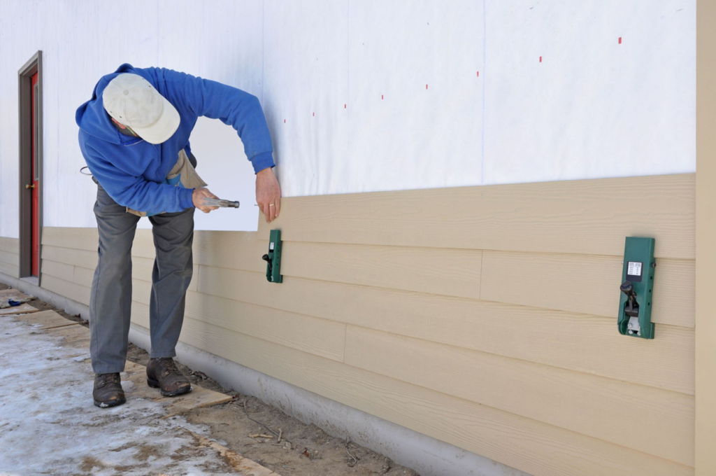 A siding contractor installing light-colored horizontal siding panels on a house, demonstrating work by ING Contractors LLC in Cary, NC.
