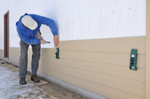 A siding contractor installing light-colored horizontal siding panels on a house, demonstrating work by ING Contractors LLC in Cary, NC.