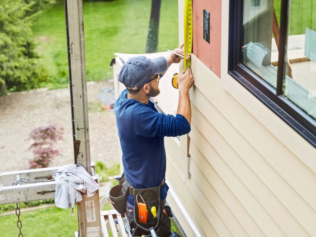 A siding contractor measuring and marking siding panels on a house by Ideal Siding Dallas, TX.