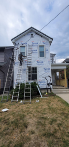 A siding contractor working on a house wrapped in Tyvek HomeWrap with ladders, performing siding installation in Columbus, OH.